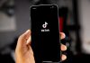 TikTok pregătește plățile peer-to-peer în mesajele directe A hand holding a smartphone displaying the TikTok logo on a black screen
