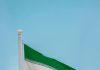 Low-angle view of the Iranian flag waving on a flagpole against a clear blue sky in Tehran, Iran.
